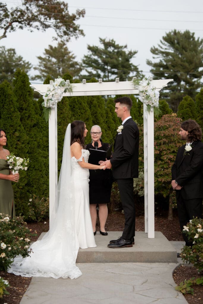 The couple exchanges vows beneath a white floral arbor during an intimate outdoor ceremony with a CT wedding photographer perspective.