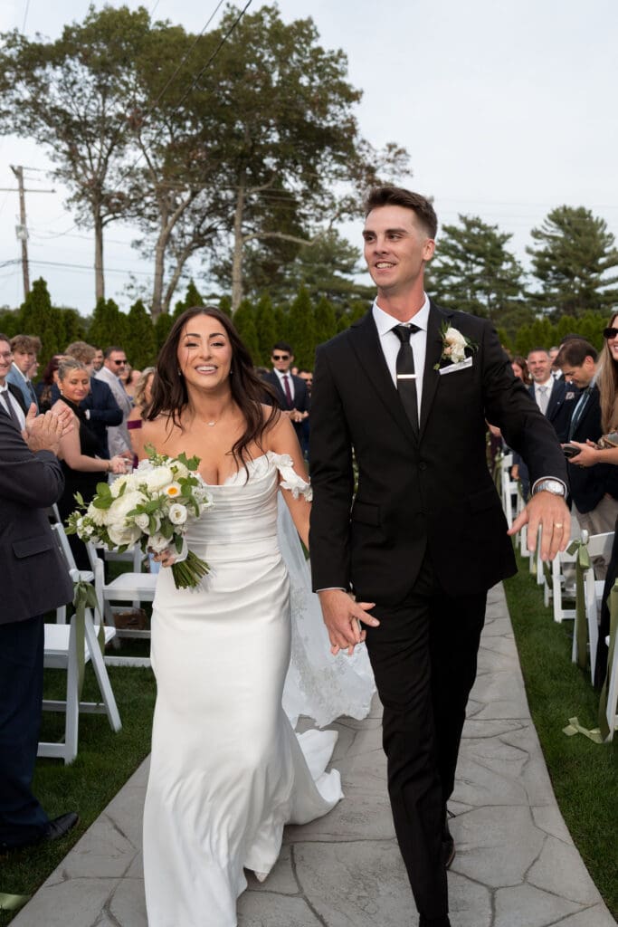 The couple walks back up the aisle smiling as guests look on after the ceremony, captured in a bright, joyful moment by Wedding Photographers CT.