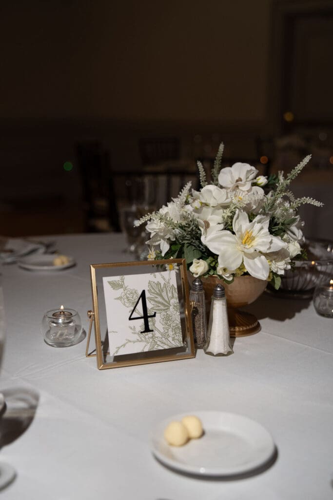 A white floral centerpiece and table number sit on a softly lit reception table, photographed with the detail-focused eye of a wedding photographer in CT.