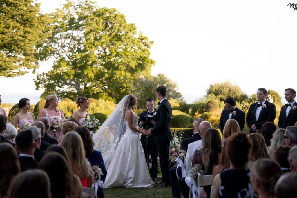 The bride and groom stand at the altar during their outdoor ceremony, surrounded by guests and late-day sun at one of the most scenic Connecticut wedding venues.