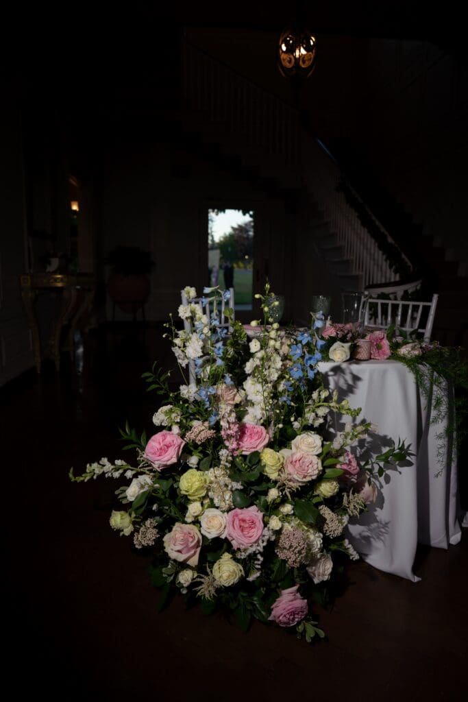 A lush floral arrangement stands in the dim reception space with the staircase beyond, styled as a romantic detail by a wedding photographer in Connecticut.