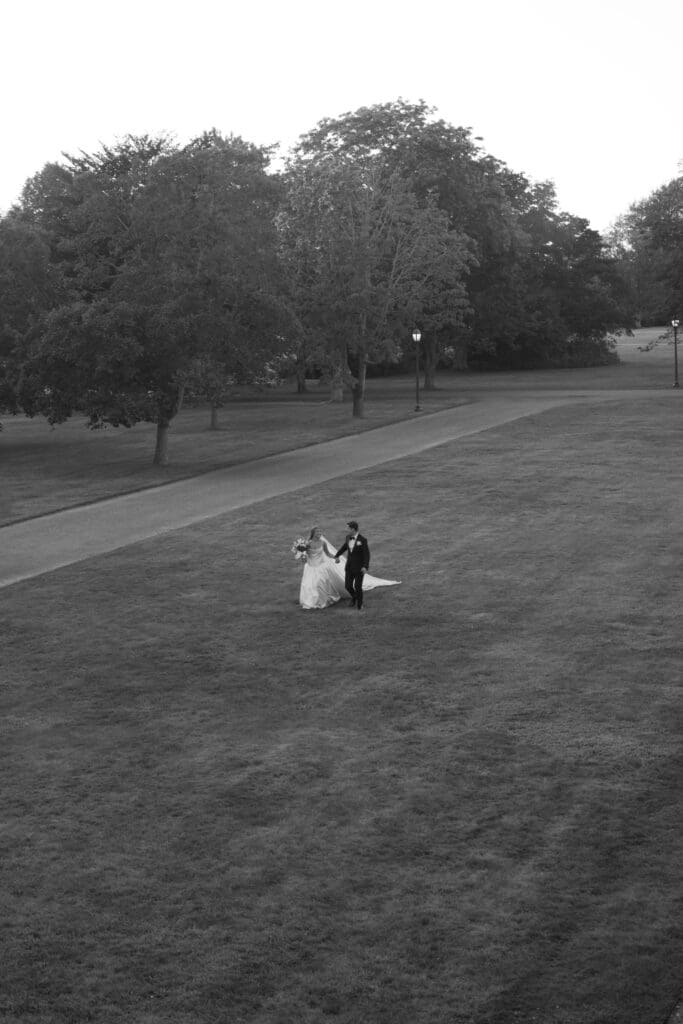 From far across the lawn, the couple appears small against the sweeping grounds in a cinematic black-and-white view of a Connecticut estate wedding venue.