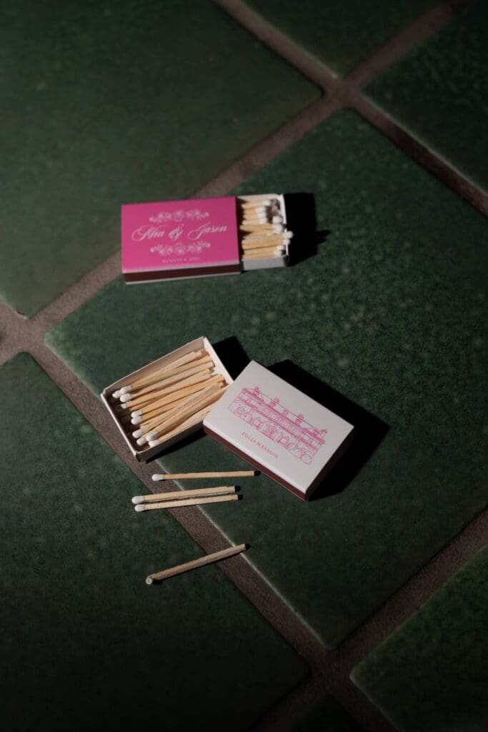 Custom matchboxes are styled on dark green tile for a refined detail shot from an Eolia Mansion wedding celebration.