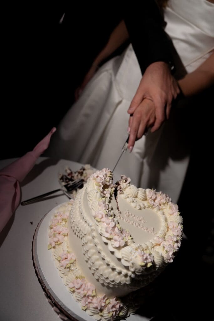 Hands meet over a heart-shaped cake as the couple begins the cake cutting, a close reception detail from wedding photographers in CT.