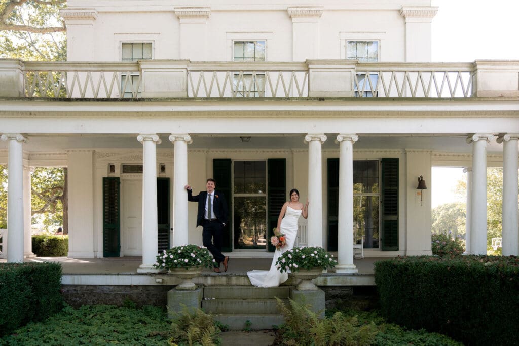 Framed by the mansion’s white columns, the bride and groom stand on the front steps in a classic portrait from one of the best estate wedding venues in Connecticut.