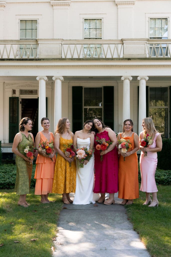 The bride and her bridesmaids gather in bright, colorful dresses outside the mansion for a joyful group portrait at one of the best wedding venues in Connecticut.