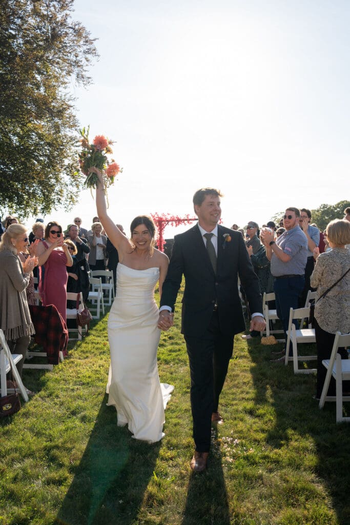 Just married, they walk back up the aisle smiling as guests cheer on the lawn at one of the best outdoor wedding venues in Connecticut.