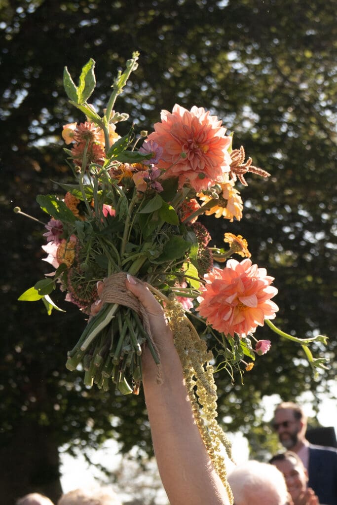 A bouquet of coral and blush blooms is lifted into the evening light beneath the trees at a romantic outdoor wedding venue in Connecticut.