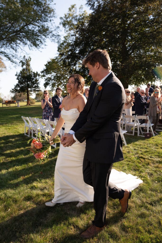 Just married, the couple walks back up the aisle smiling in golden light at one of the best outdoor wedding venues in Connecticut.