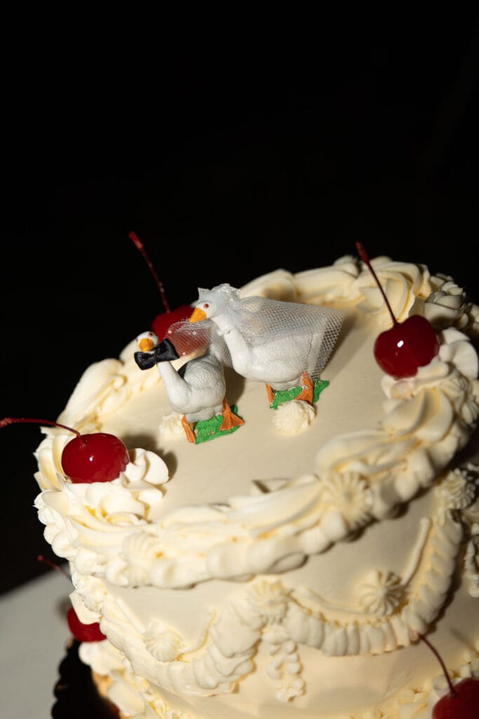 A vintage-style white cake topped with cherries and piped frosting is photographed against a dark background during the reception at a romantic Connecticut wedding venue.