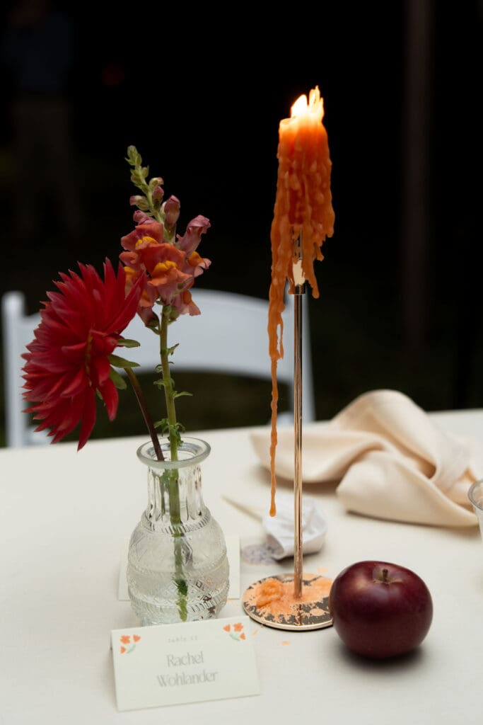 A taper candle drips onto a cream table beside a single flower and escort card in a softly styled detail from a romantic Connecticut wedding venue.
