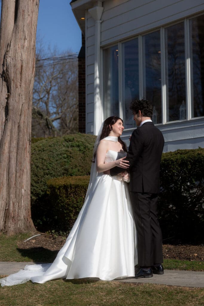 The couple stands close outside the house as late-day sun catches the bride’s veil and gown in a quiet portrait by a wedding photographer CT.