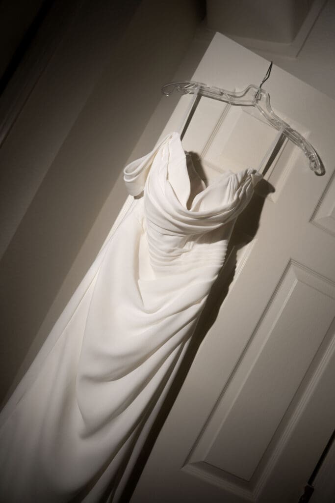 The bride’s gown hangs in angled window light against a paneled door, photographed as a classic getting-ready detail for a Wadsworth Mansion wedding photographer feature.
