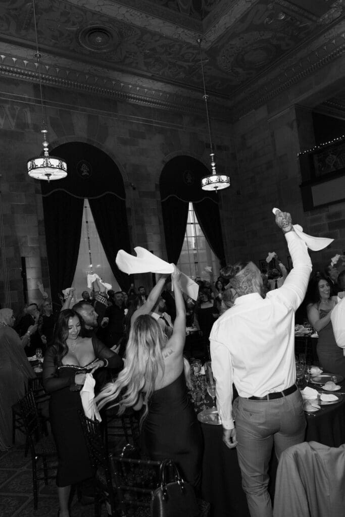 Guests cheer and wave napkins on the dance floor beneath soaring ceilings during a lively reception captured by a Connecticut editorial wedding photographer.