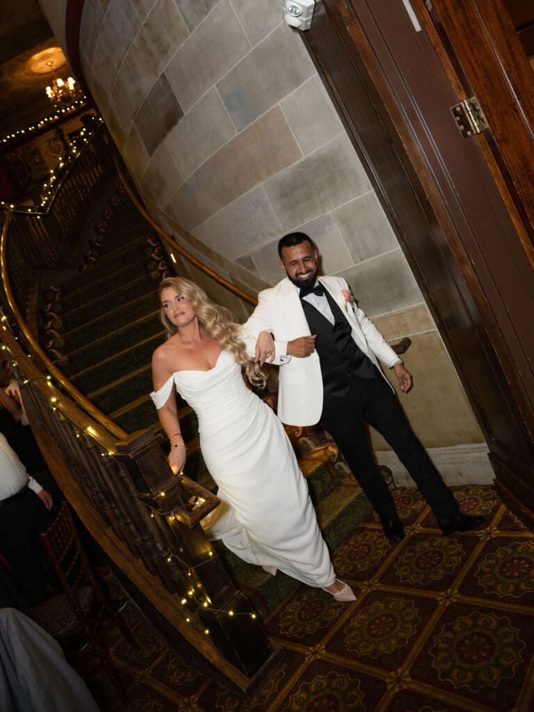 The bride and groom descend the staircase together, framed by stone walls and glowing rail lights in a moment suited to a CT wedding photographer editorial.