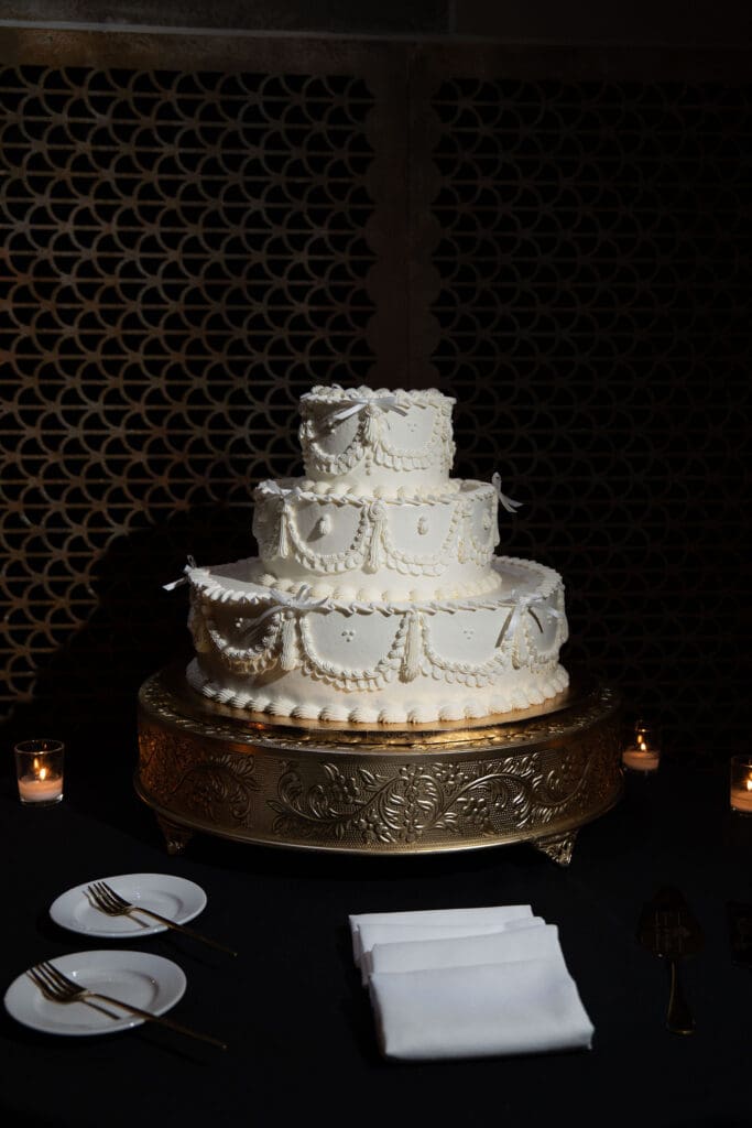 A tiered white cake sits on an ornate stand against a dark backdrop, captured as an elevated detail from a timeless Wadsworth Mansion wedding.