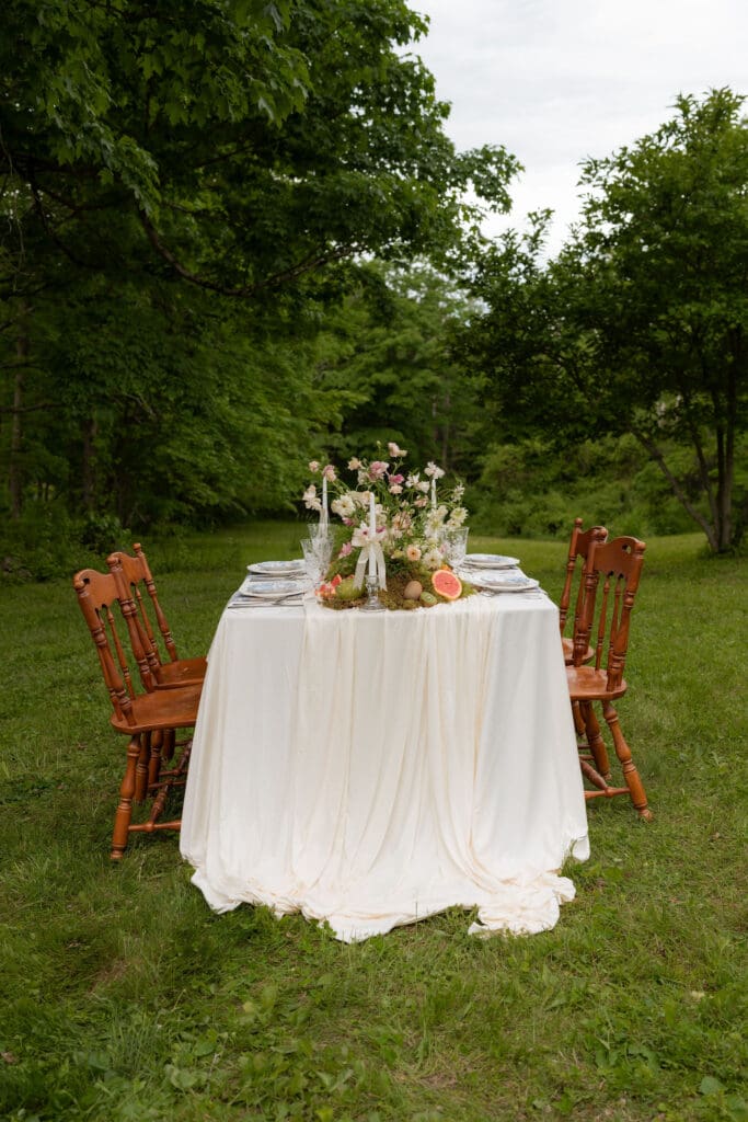 A draped reception table stands alone on the grass surrounded by trees, capturing the quiet beauty of a Connecticut outdoor estate wedding venue.