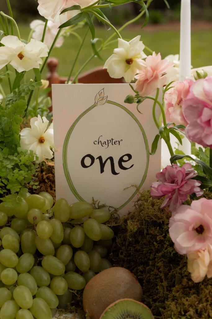 A chapter one table marker sits among grapes, moss, and pastel flowers in a styled reception detail at a garden wedding venue Connecticut couples love.