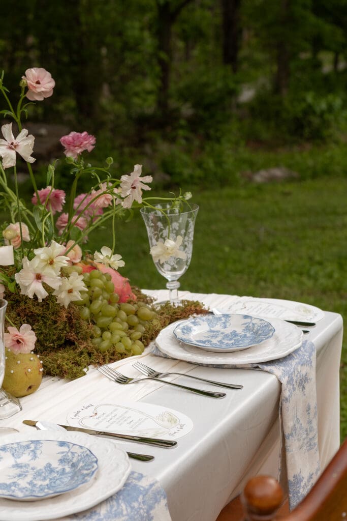 Blue-and-white place settings, garden flowers, grapes, and glassware are styled across an elegant outdoor tablescape by a Connecticut wedding photographer guide.