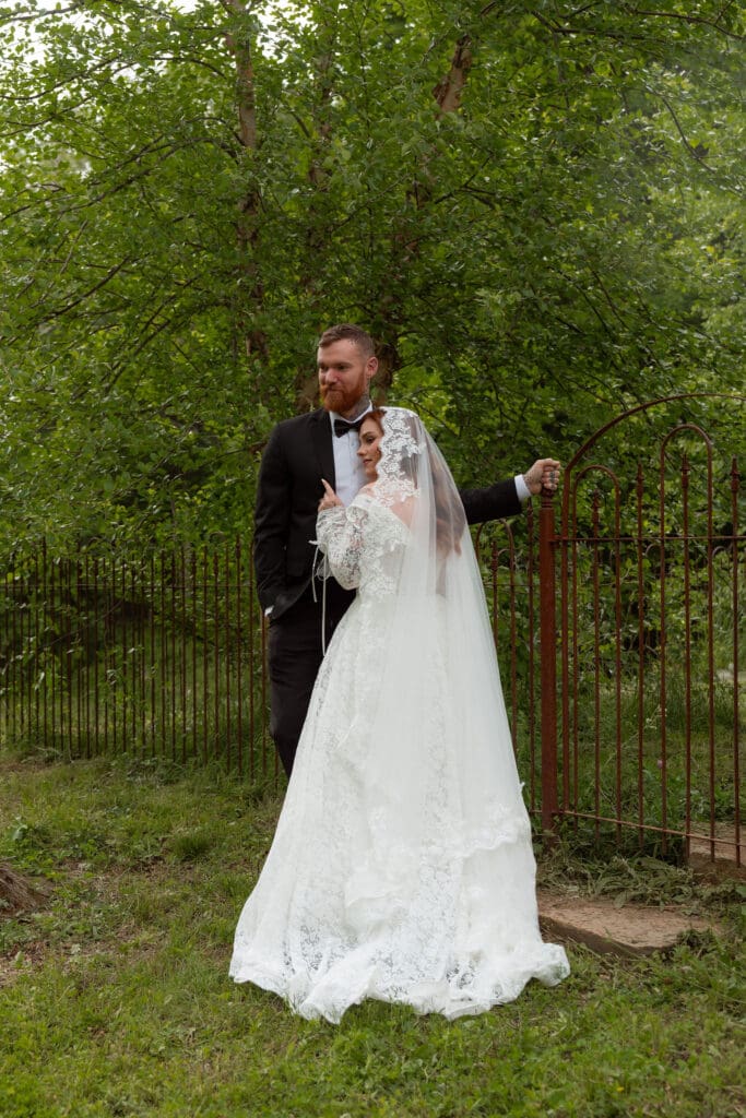 Framed by greenery and an iron gate, the couple pauses together for a quiet portrait from a wedding photographer in CT.
