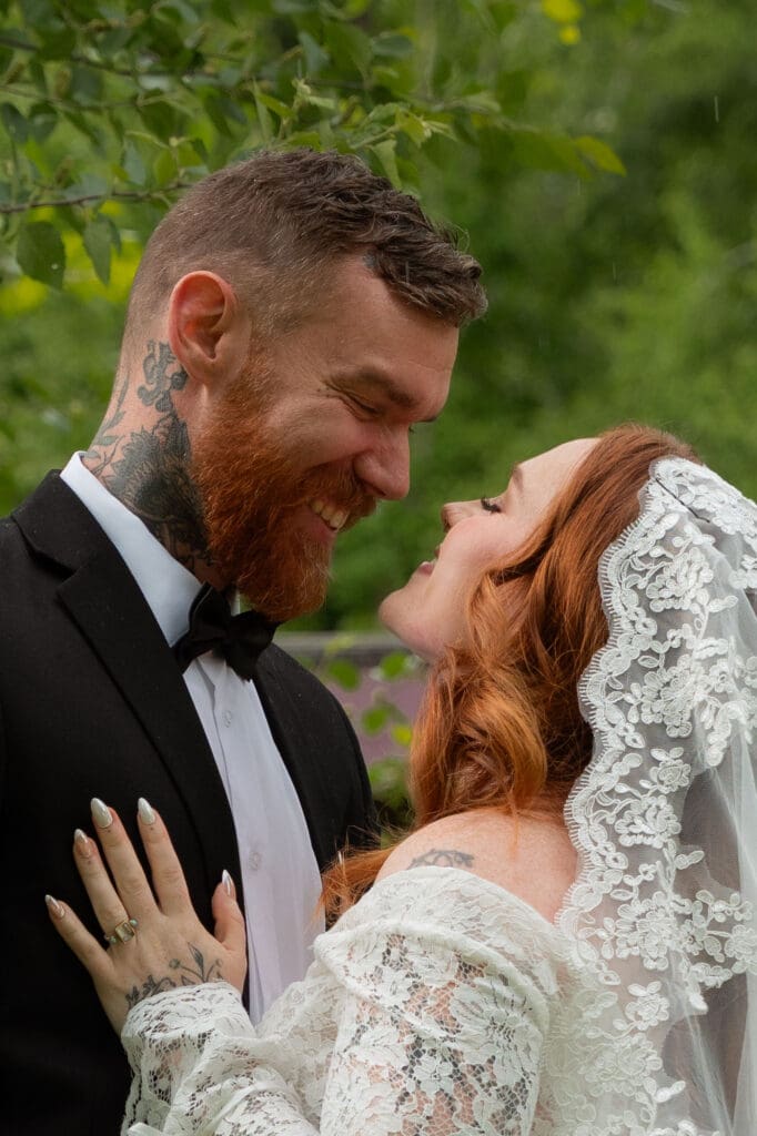 The groom smiles down at the bride as she looks up at him beneath her lace veil, photographed for naturally connected images by CT wedding photographers.