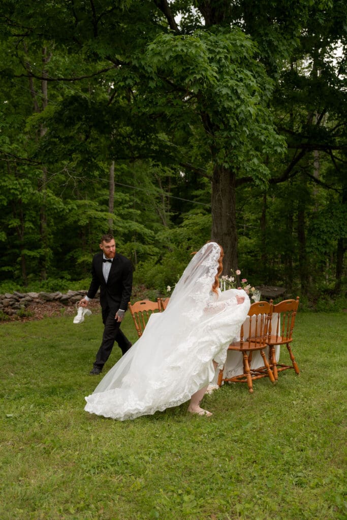 The groom leads the bride past the dinner setup as her lace gown trails across the grass at this Connecticut estate wedding photographer setting.