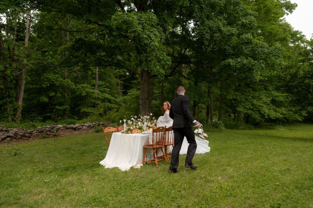 The groom walks toward the bride beside an intimate reception table set in the woods at a wedding venues outdoors Connecticut celebration.