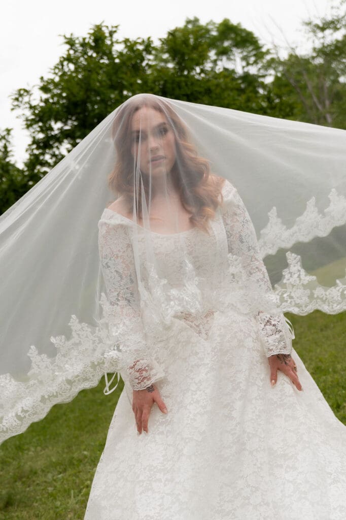 Framed beneath her lace-edged veil, the bride stands on the grass in a soft portrait from a romantic Wadsworth Mansion wedding.